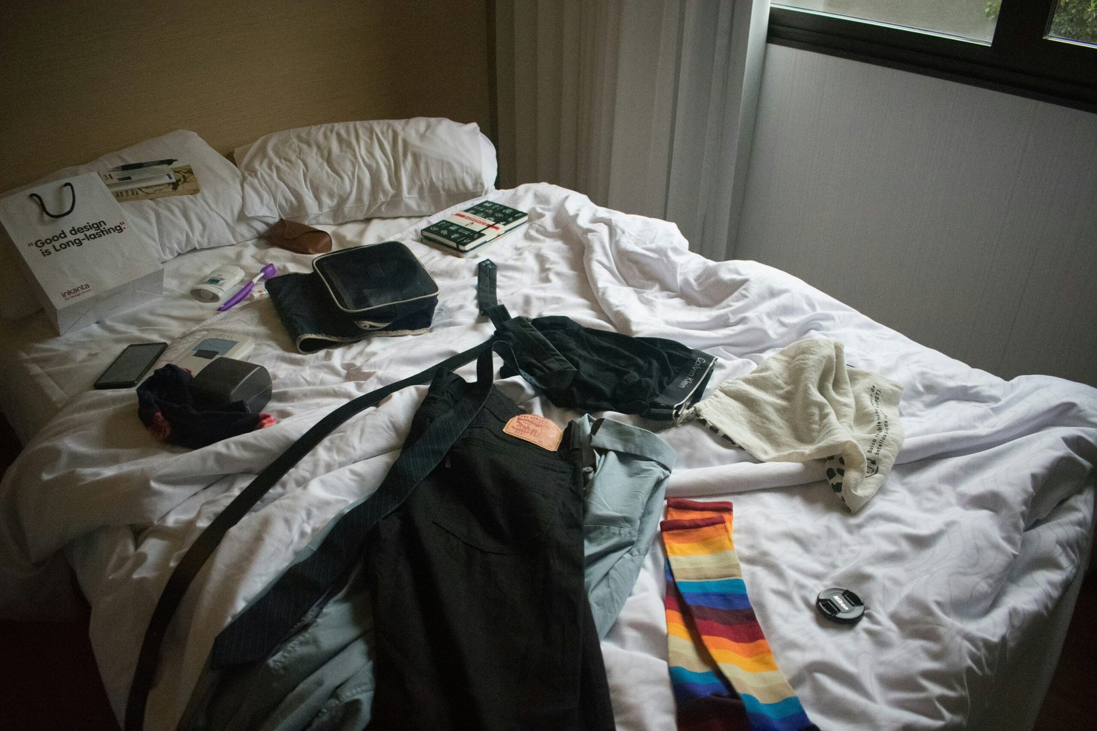 Kleidung liegt ruhig ausgebreitet auf einem Bett bei neutralem Licht.